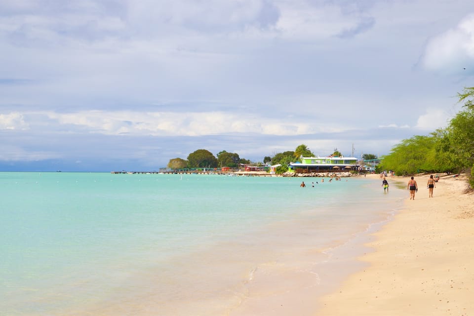 A beach with turquoise water, a pier, and a few people walking along the shore.