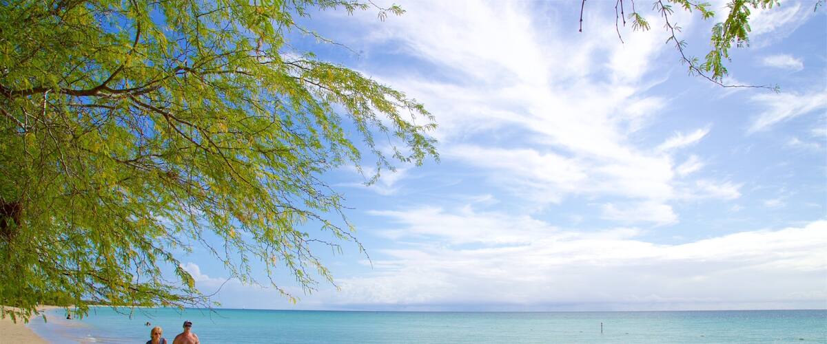 A beach with clear turquoise water and a few people walking along the shore.