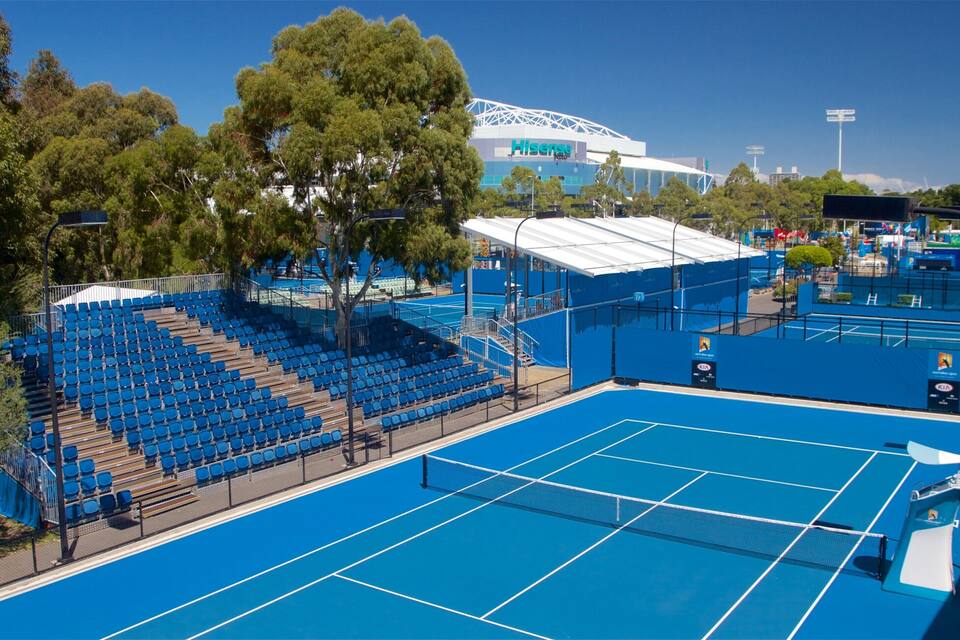 A tennis court with blue seating and a large stadium in the background.