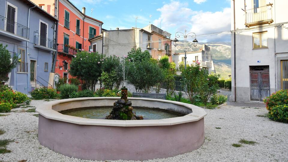 A fountain in a courtyard surrounded by colorful buildings and greenery.