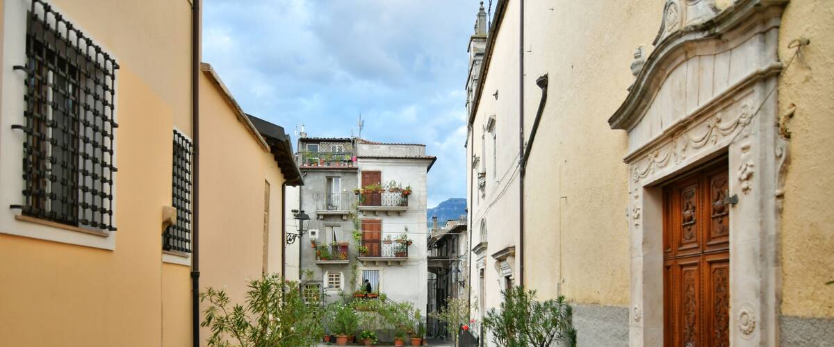 A cobblestone street flanked by buildings with balconies and potted plants.