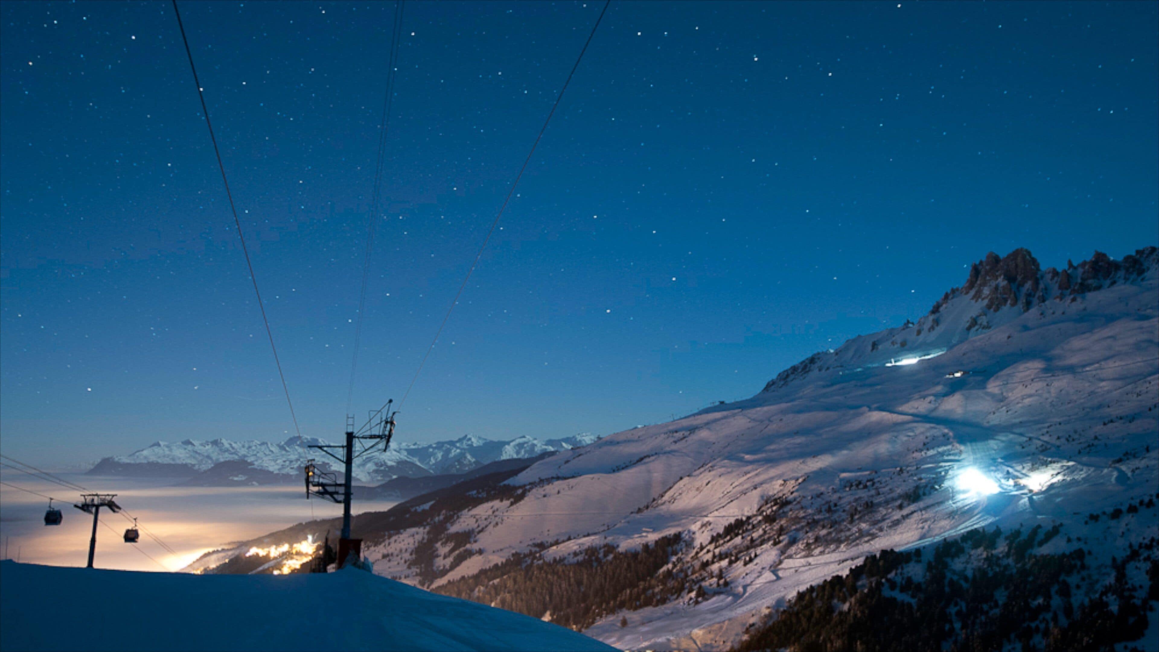 A snowy mountain landscape at twilight with ski lifts and a clear night sky.