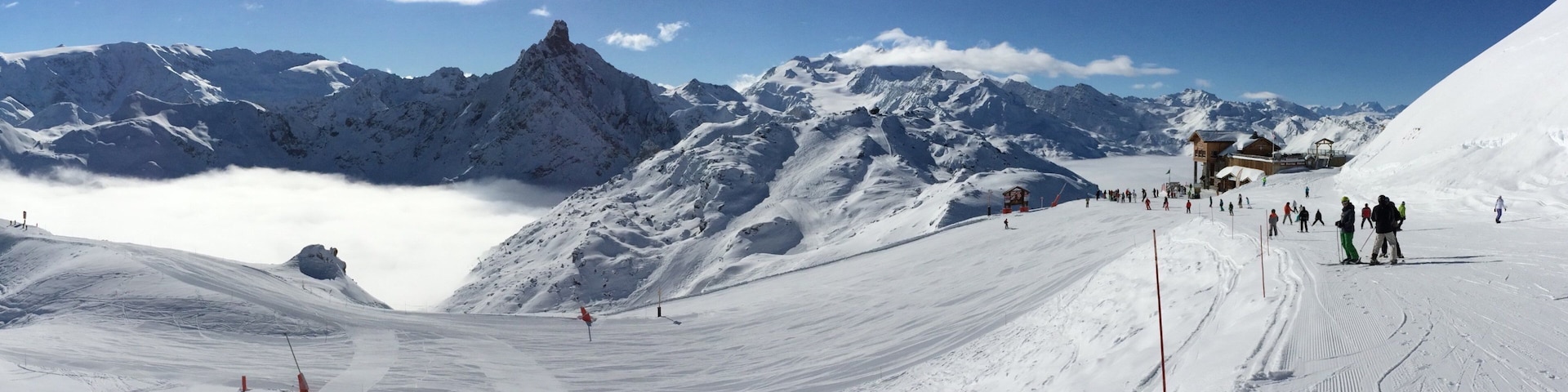 Pista de esqui coberta de neve, esquiadores, pico de montanha e céu azul límpido.
