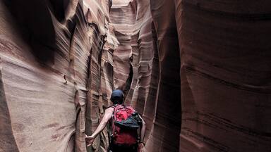 A hiker in a narrow canyon with layered rock walls.