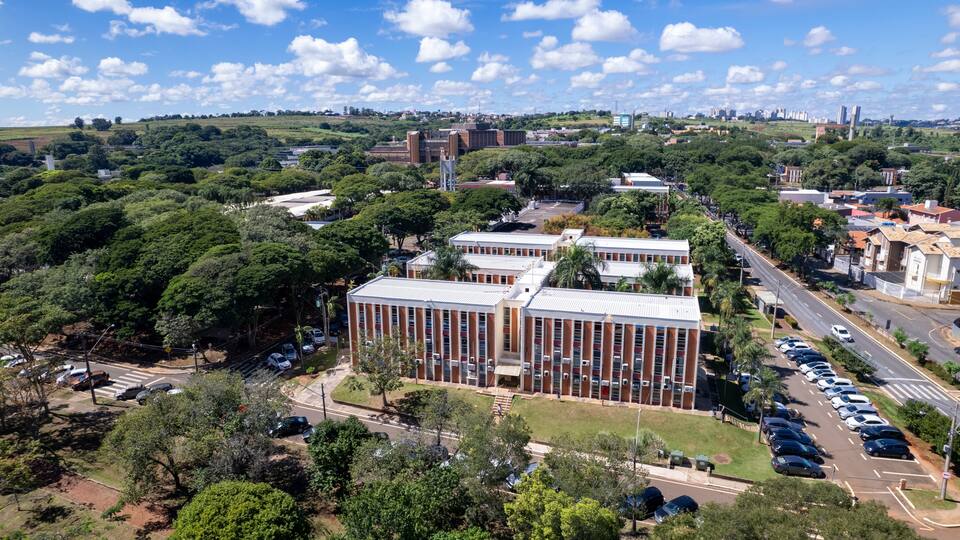 An urban landscape with a prominent building complex, surrounded by lush greenery and a clear blue sky.
