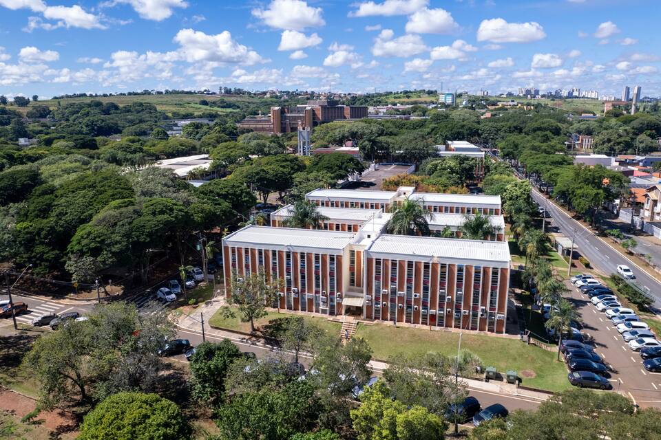 Paisagem urbana com um complexo de edifícios imponente, rodeado por vegetação exuberante e um céu azul límpido.