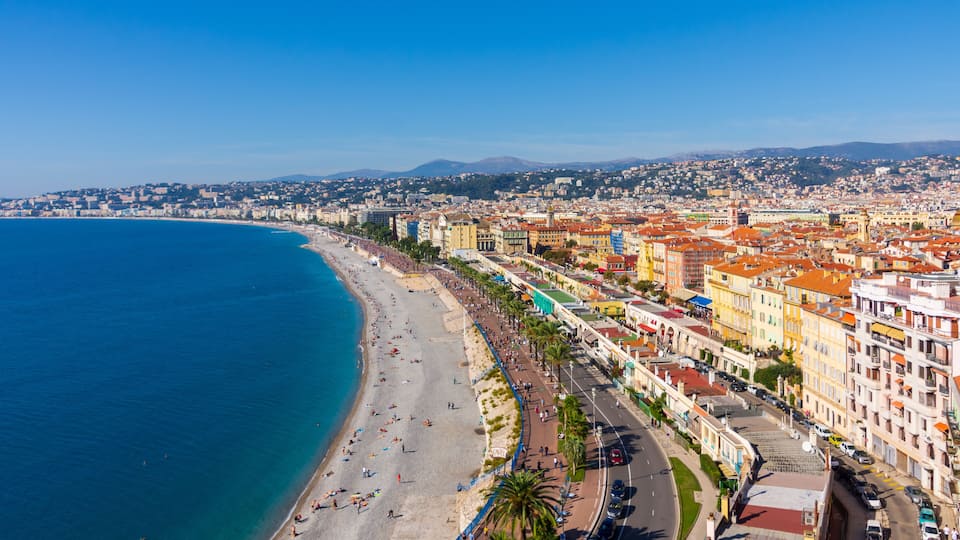 Paisagem urbana costeira com praia, calçadão com palmeiras e edifícios coloridos.