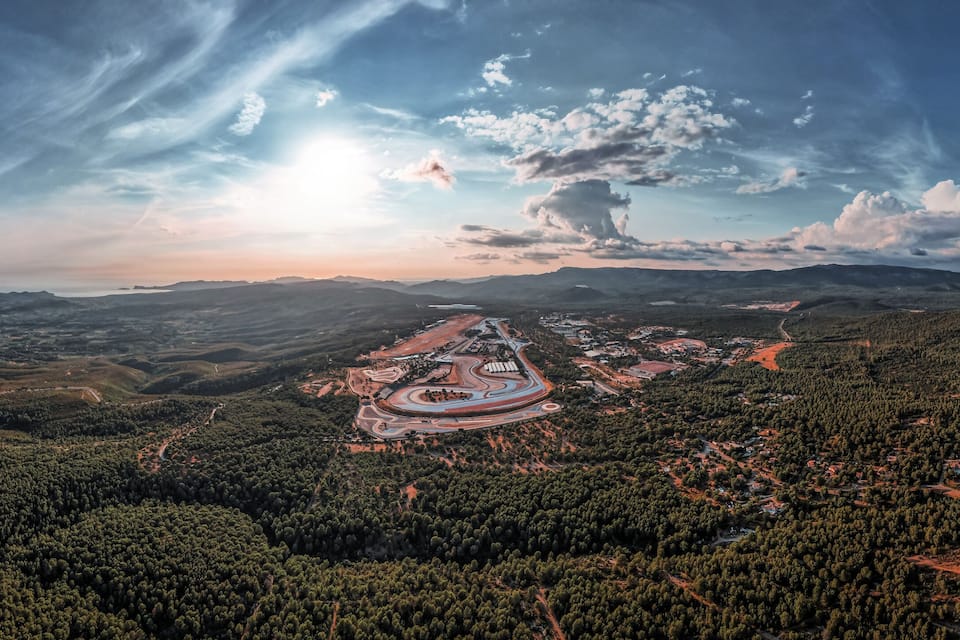 Une vue panoramique d’un paysage montagneux, avec une route sinueuse, de vastes forêts et une grande structure circulaire située dans la vallée.
