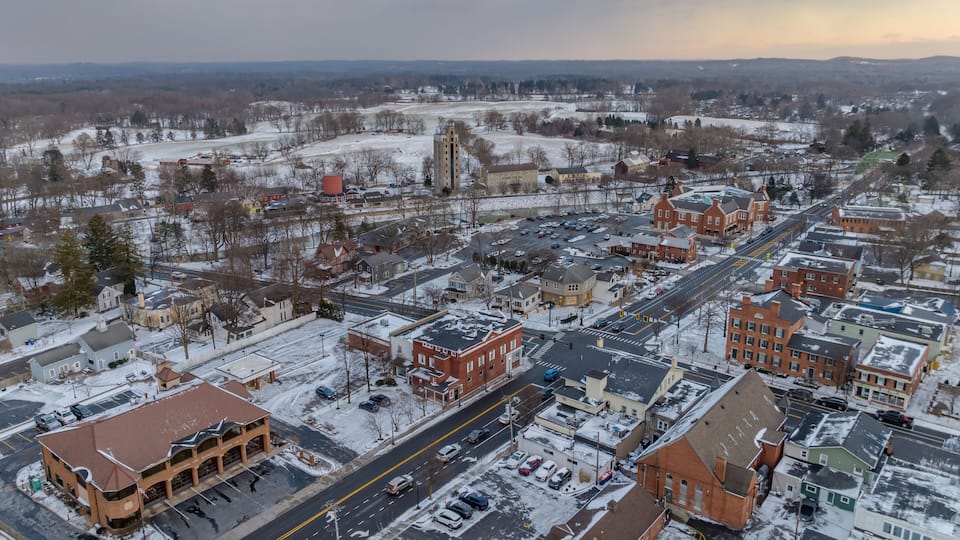 A snow-covered town with historic buildings, a prominent church steeple, and a river in the distance.