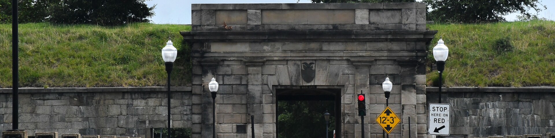 A stone archway with a 'STOP HERE ON RED' sign, a height restriction sign, and a 'MAIN GATE' sign.
