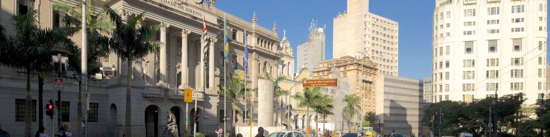 A city street with a historic building, palm trees, and modern high-rises.