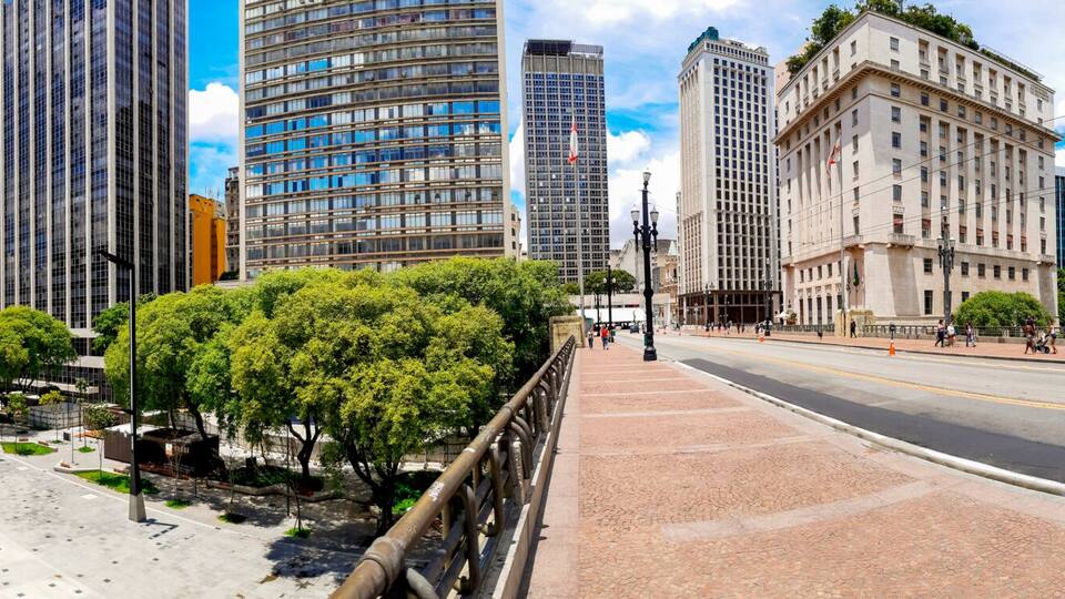 Paisagem urbana com edifícios altos, uma estrada curva e uma passarela arborizada.
