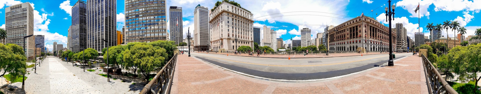 Paisagem urbana com edifícios altos, uma estrada curva e uma passarela arborizada.