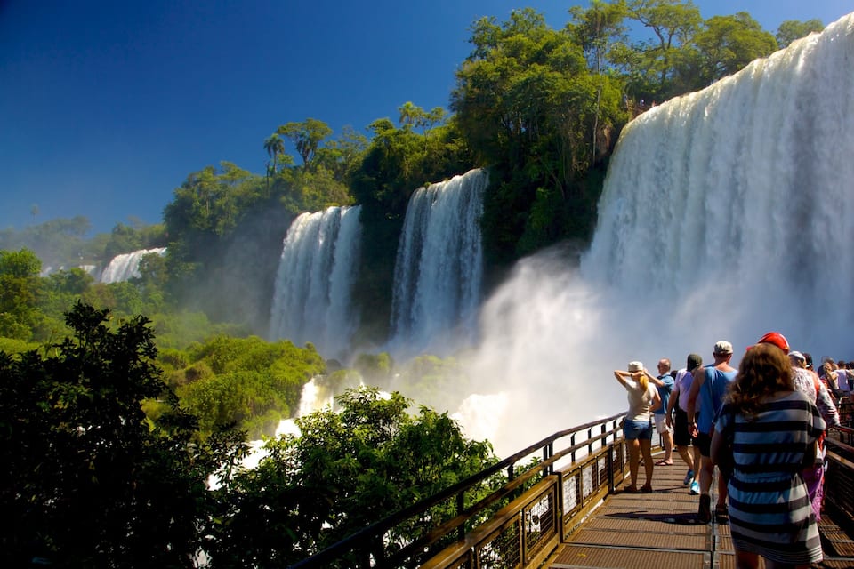 A large waterfall with multiple tiers, surrounded by lush greenery and a viewing platform with people observing.