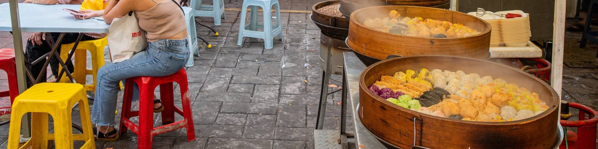 Un mercado callejero animado, con gente cenando en mesas, puestos de comida y grandes ollas de cocina.