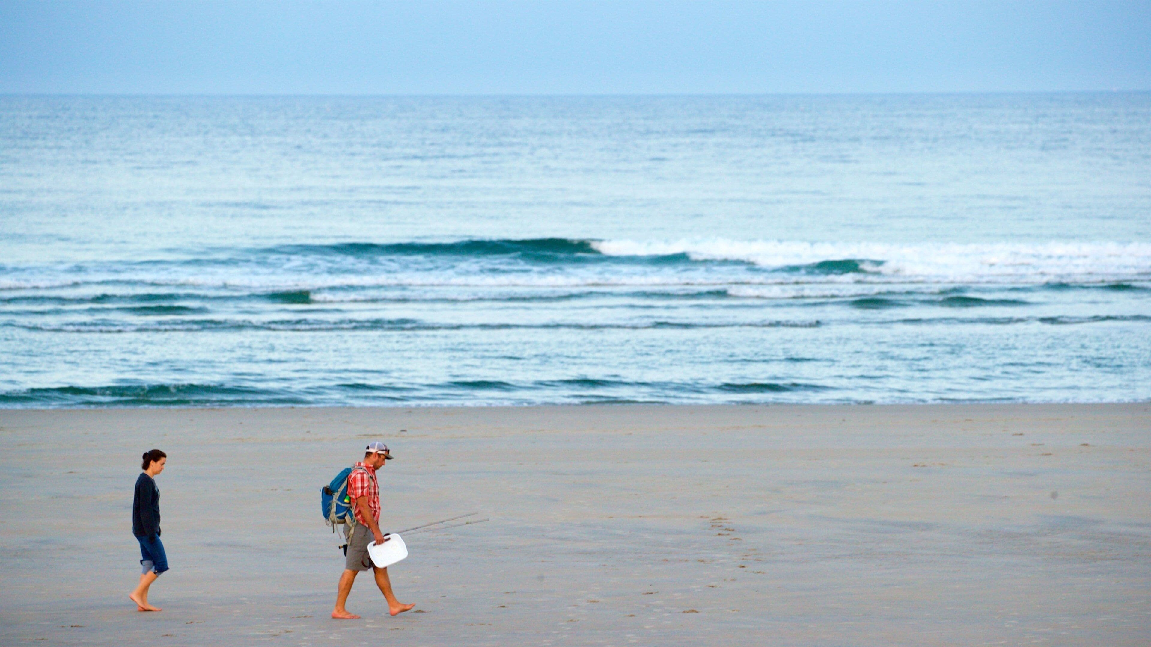A beach with a man and a child walking along the shore.