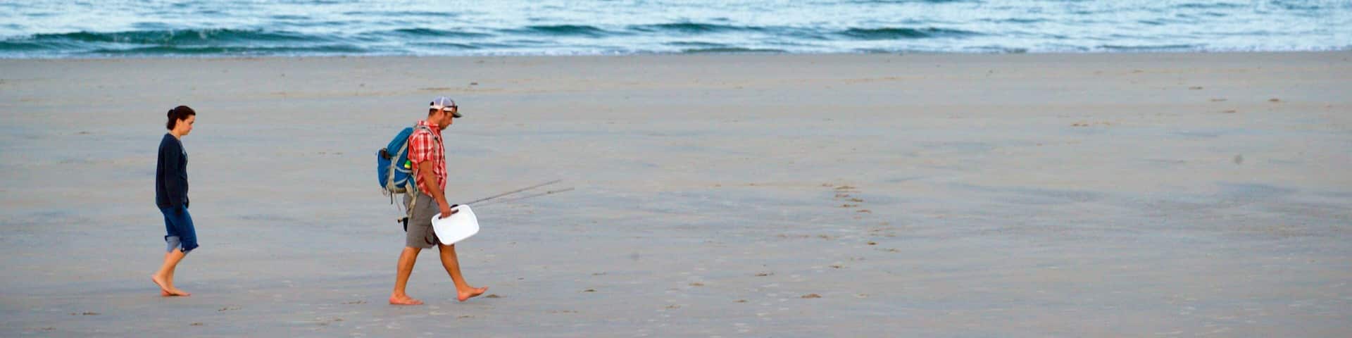 A beach with a man and a child walking along the shore.