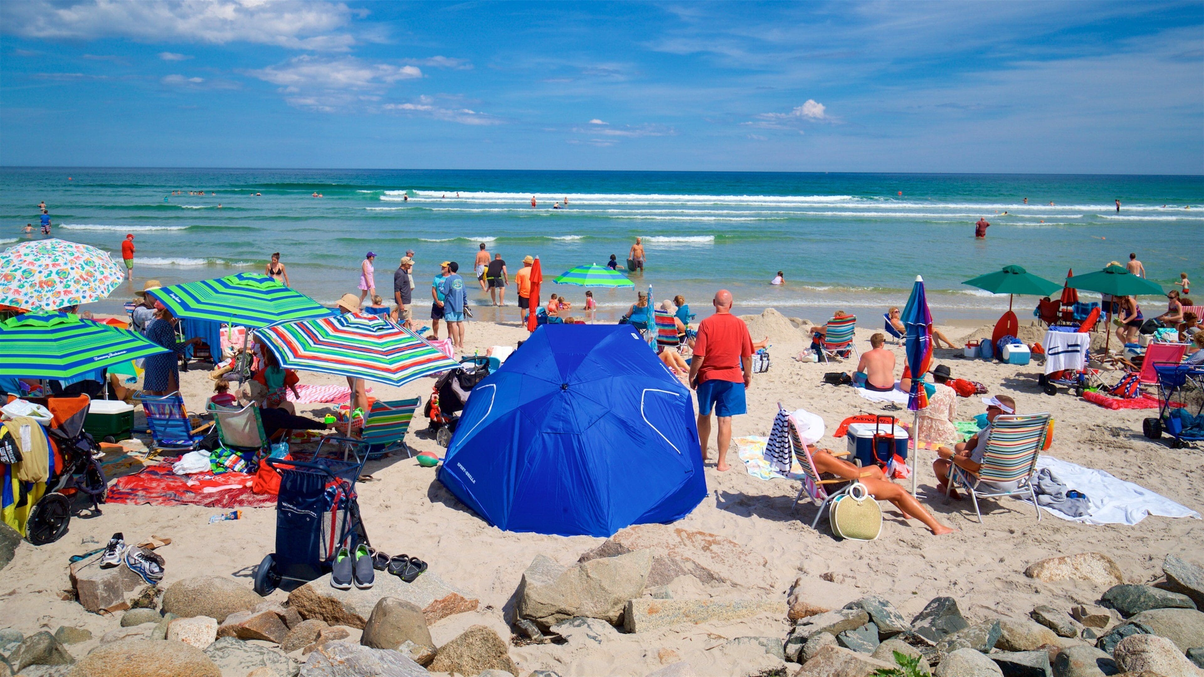 A crowded beach with people sunbathing, umbrellas, and a blue tent.