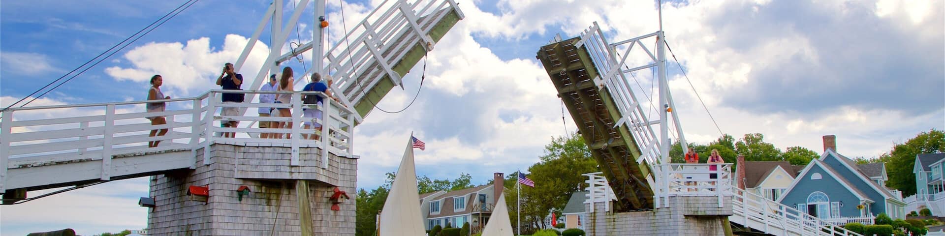 A waterfront with wooden structures, sailboats, and a bridge.