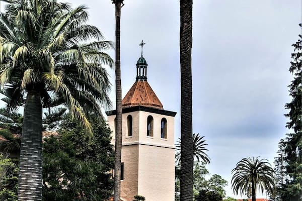 A church with a bell tower, surrounded by palm trees and a well-maintained lawn.