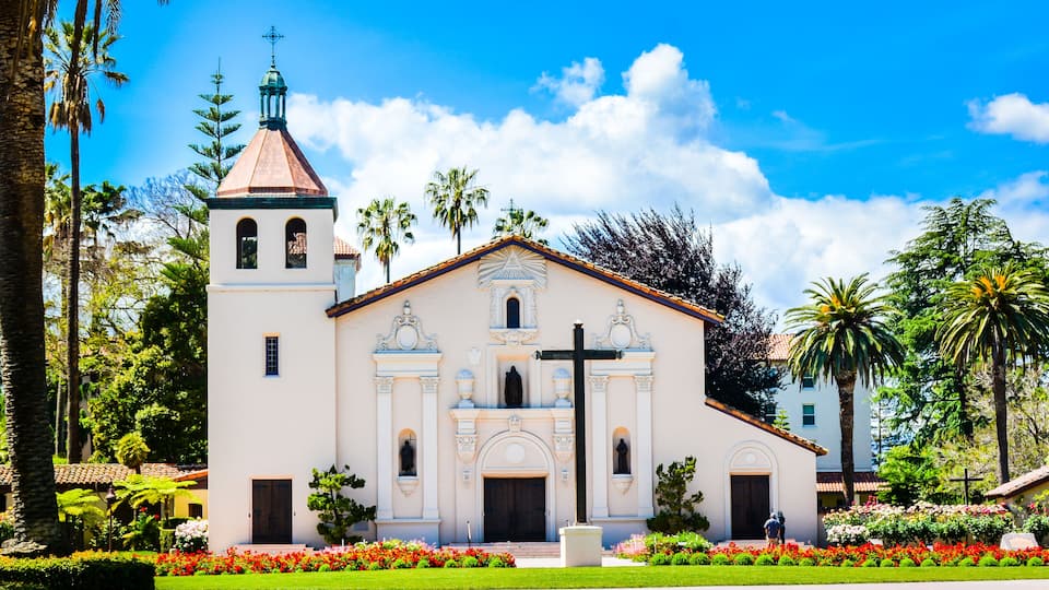 A church with a bell tower, surrounded by palm trees and a well-maintained garden.