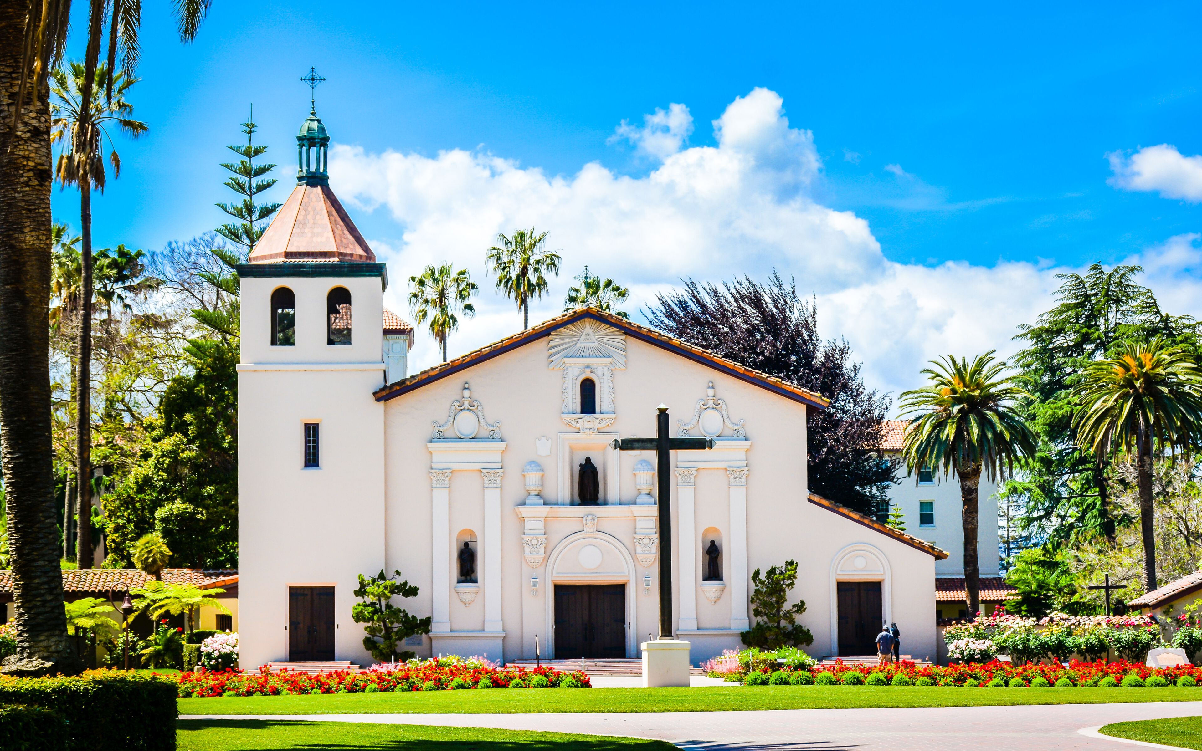 A church with a bell tower, surrounded by palm trees and a well-maintained garden.