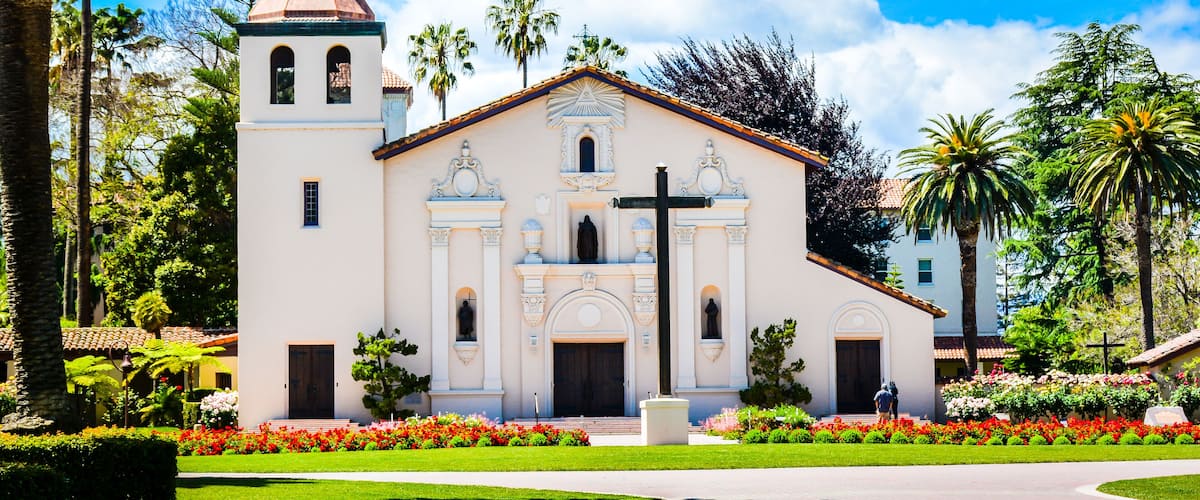 A church with a bell tower, surrounded by palm trees and a well-maintained garden.
