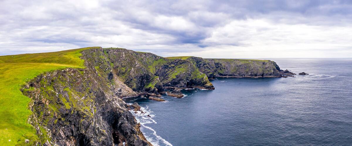 A rugged coastline with steep cliffs and a grassy plateau.