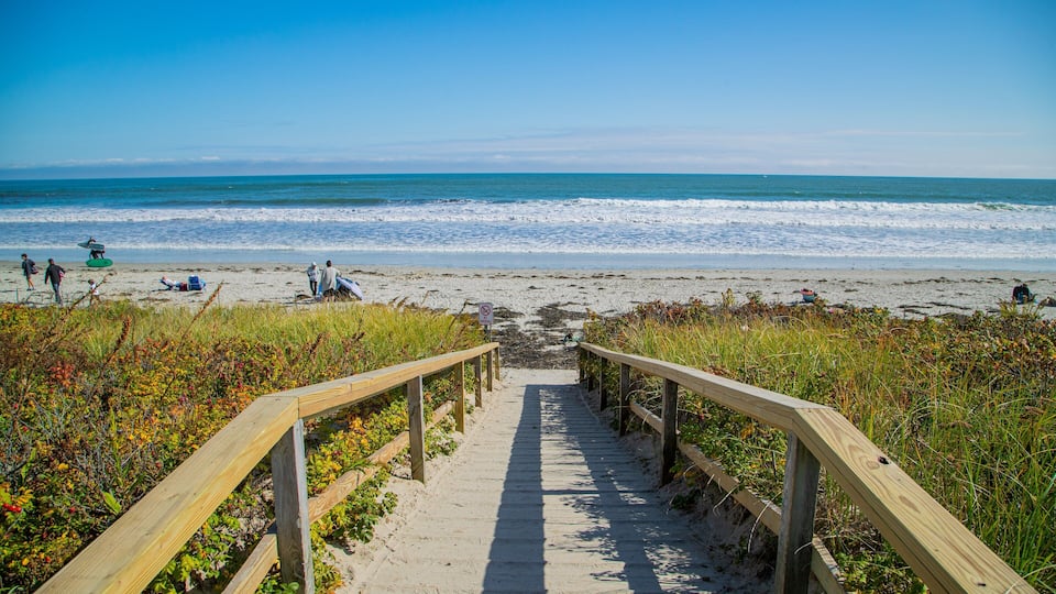 A wooden boardwalk leading to a beach with people and surfboards.