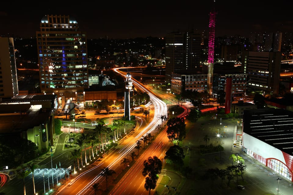 A nighttime cityscape with illuminated roads, a prominent tower, and modern buildings.