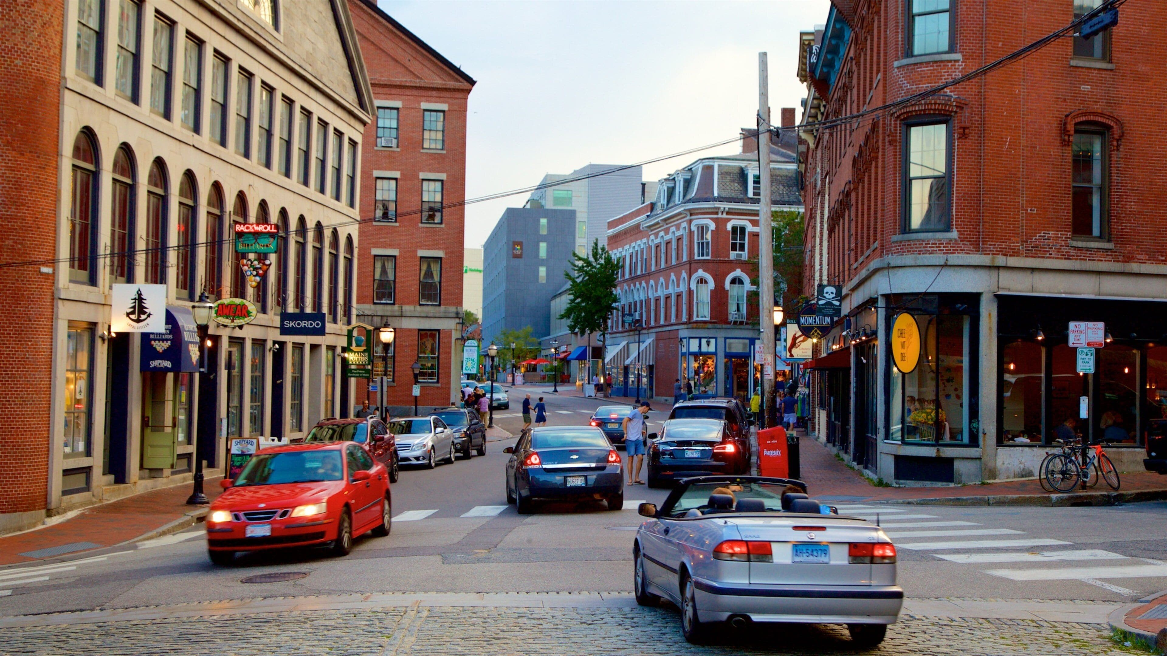 A cobblestone street lined with historic buildings, cars, and a cyclist.