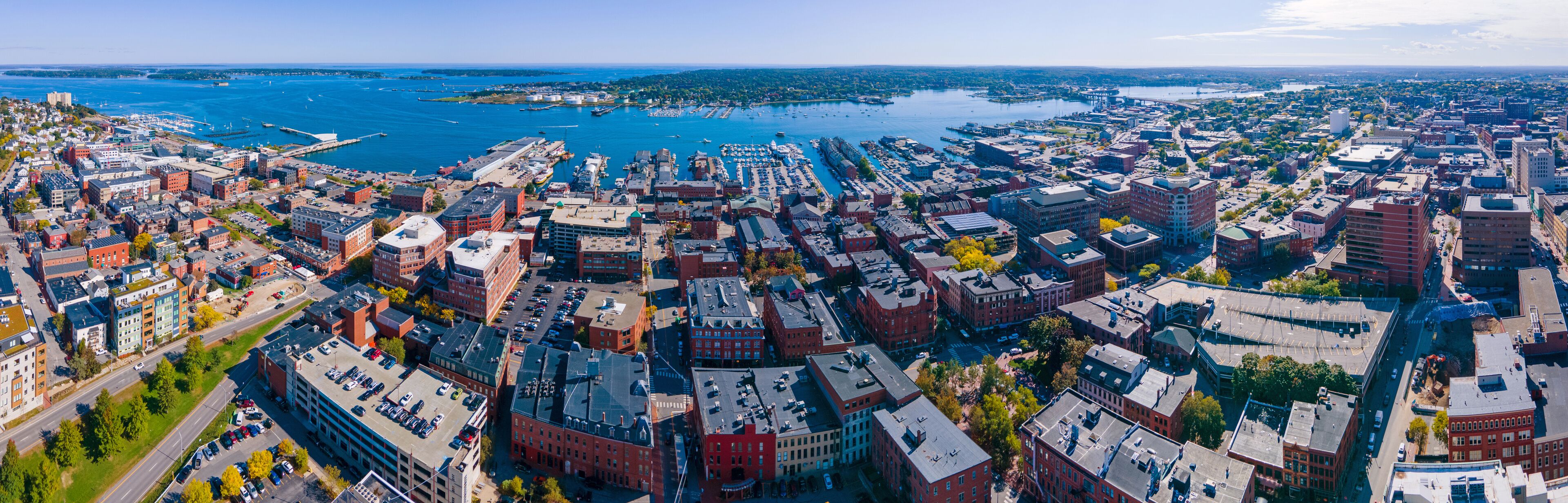 An aerial view of a coastal city with dense urban development, a marina, and a large body of water.