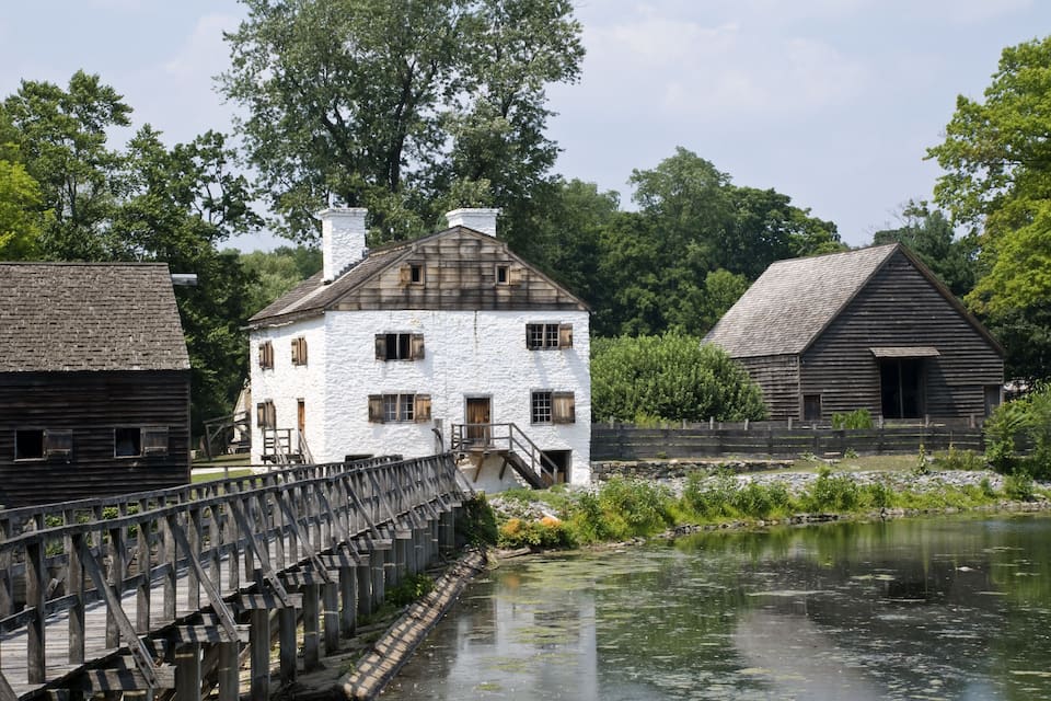Een wit huis met een houten terras en een houten brug over een rivier.