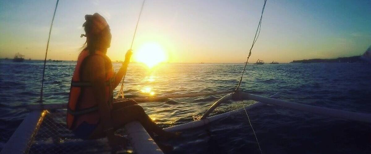 A person on a boat during sunset with the sun low on the horizon.
