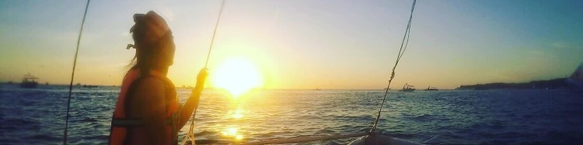A person on a boat during sunset with the sun low on the horizon.