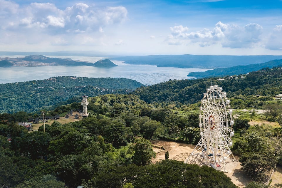 Un paysage côtier pittoresque, avec une grande roue bien visible, une végétation luxuriante et des montagnes à l’horizon.