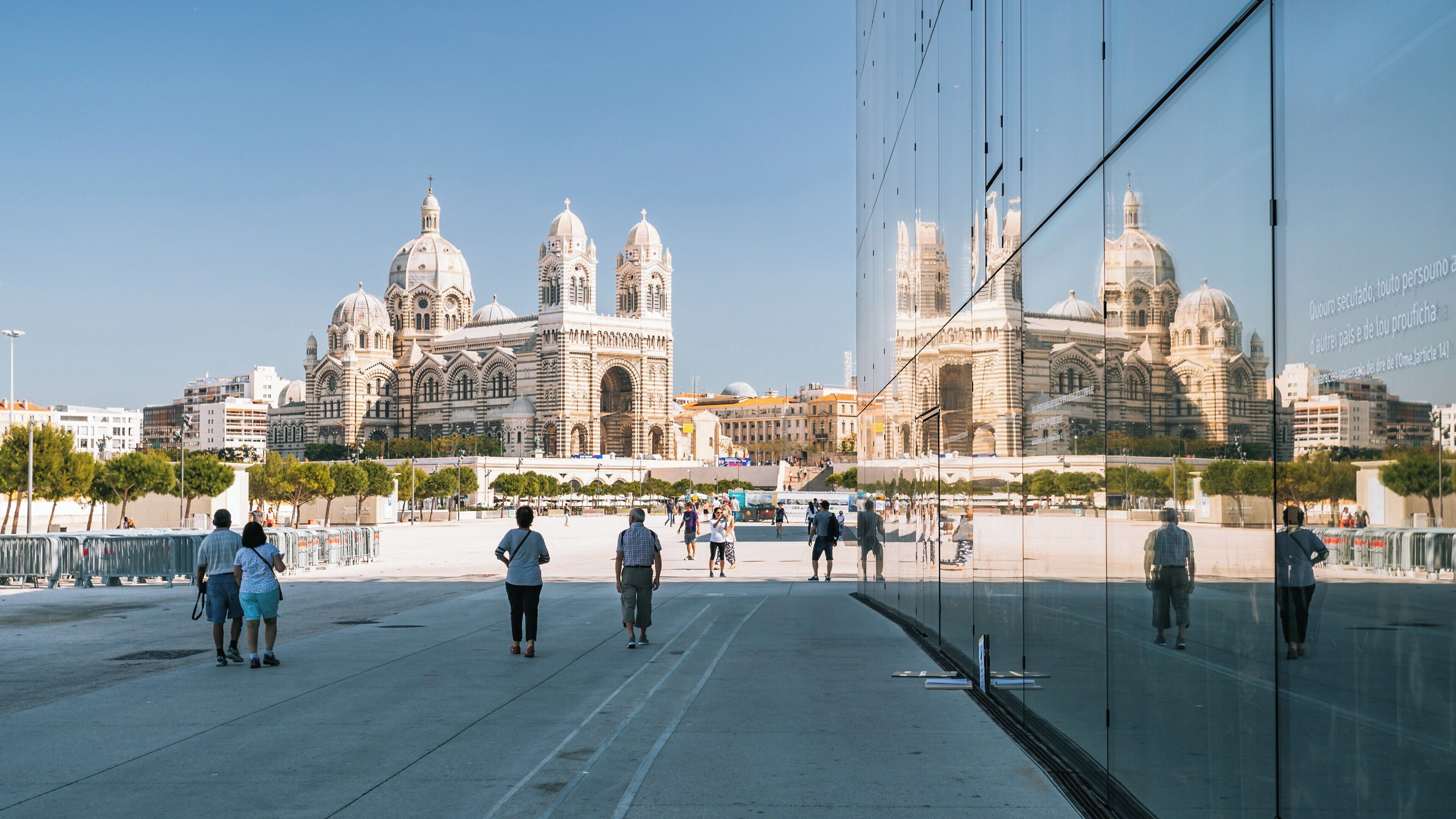 Visitors explore the Museum of European and Mediterranean Civilisations in Marseille with stunning reflections in the glass facade on a clear day