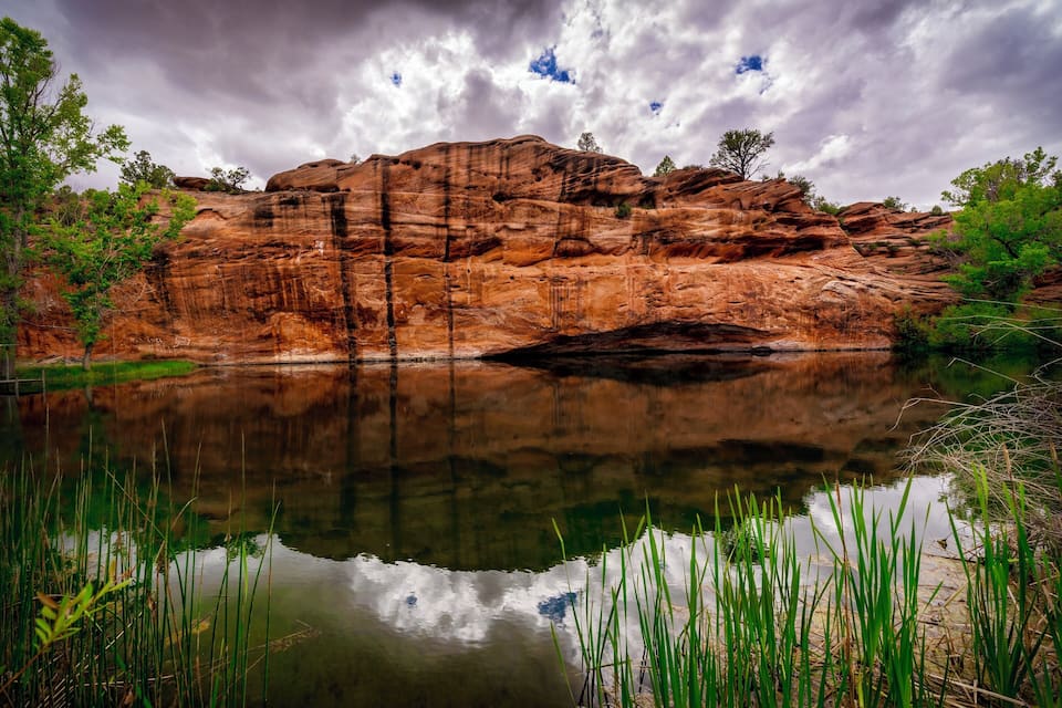 Um penhasco rochoso com um lago calmo refletindo o céu.