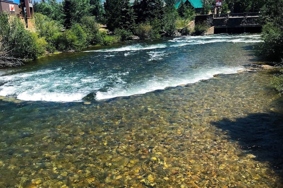 A clear river with visible rocks and a bridge in the background.