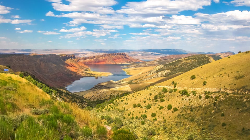A canyon with a lake, green vegetation, and distant mountains.