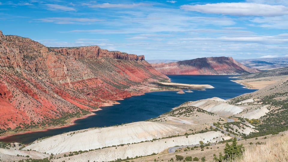 A canyon with red rock formations, a large body of water, and a winding road.