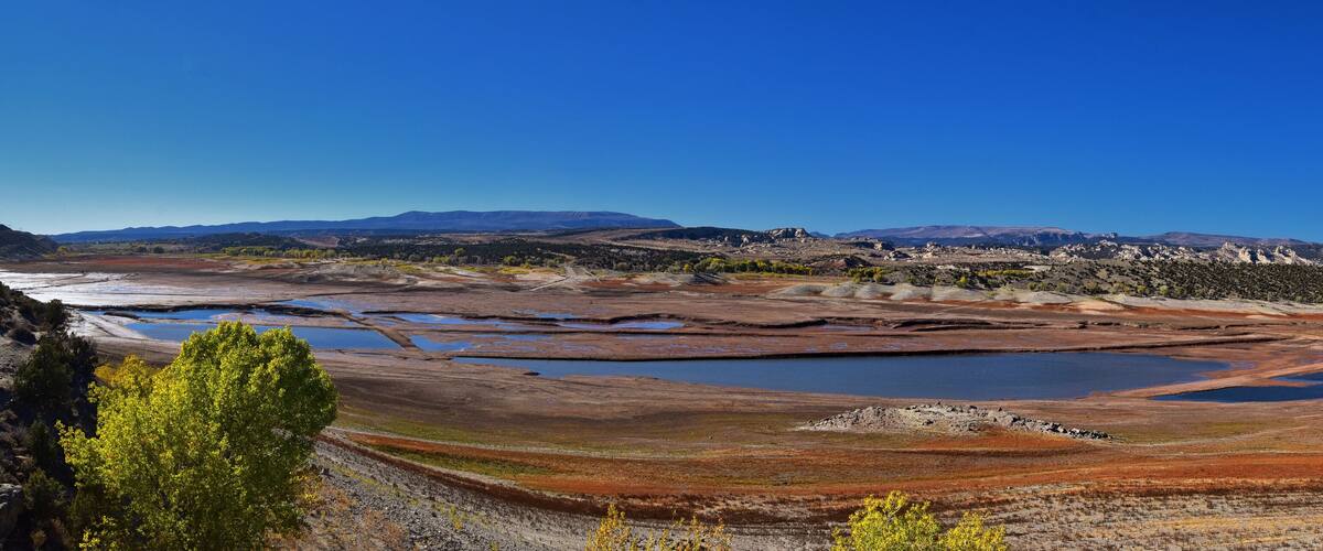 A vast salt flat with scattered water bodies and distant mountains under a clear blue sky.