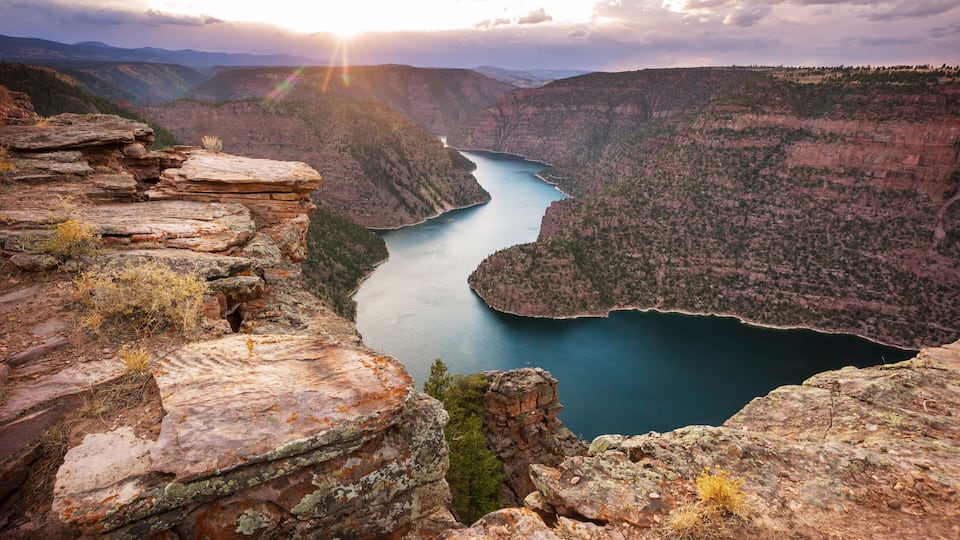A canyon with a river, rocky cliffs, and a sunset.