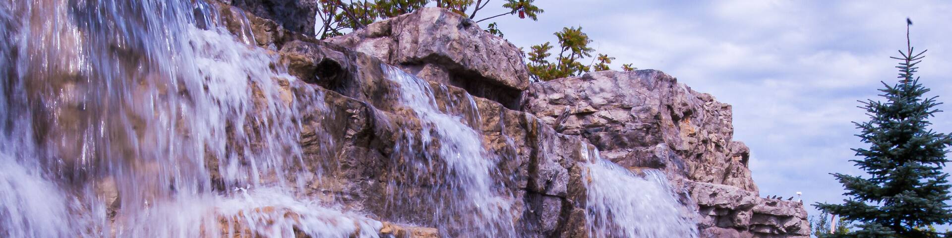 A multi-tiered waterfall cascading over rocky terrain with a coniferous tree in the background.
