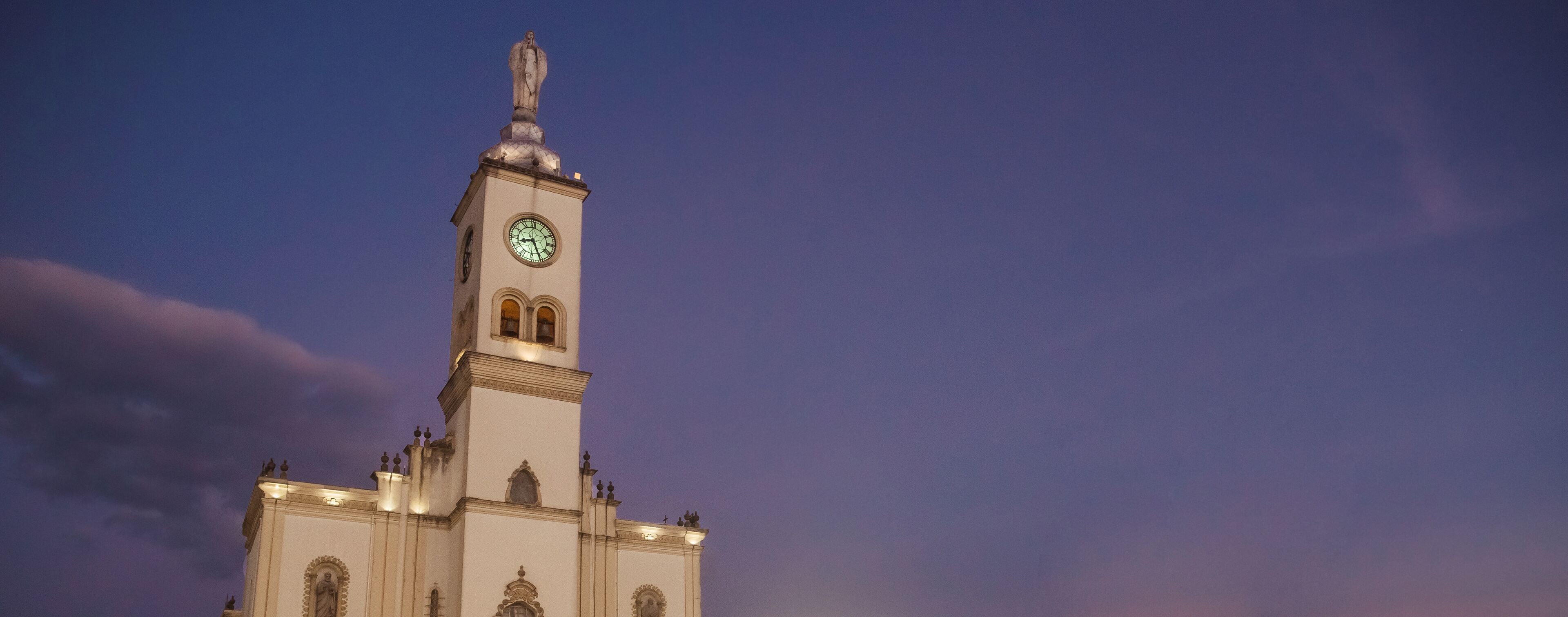 A tall white church with a clock tower against a twilight sky.