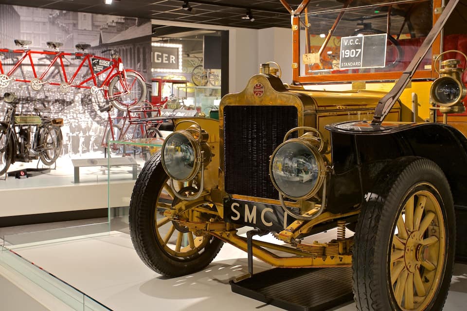 A vintage car with the license plate "SMOV" and a red bicycle in the background.