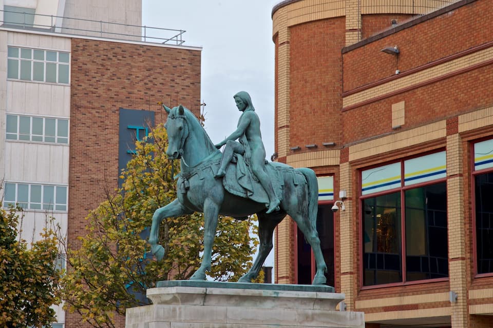 A bronze statue of a man on horseback in front of a building with a brick facade and large windows.