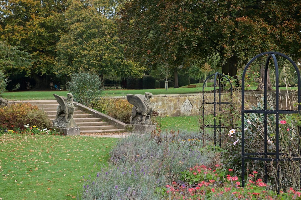 A garden with a statue of a winged creature, a metal gate, and a stone staircase.