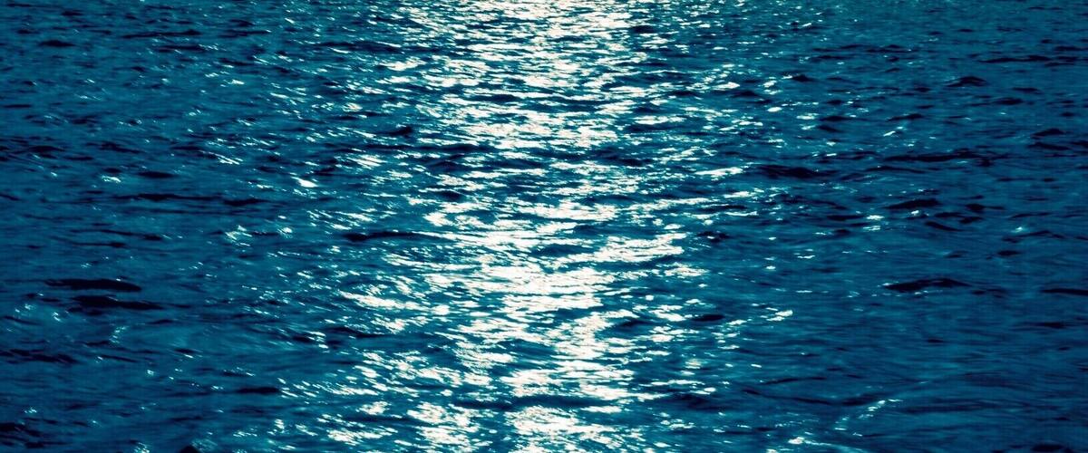 A mountain silhouette with a sun reflecting on water.