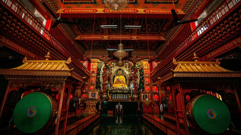 An ornate temple interior with a central statue, intricate carvings, and a chandelier.